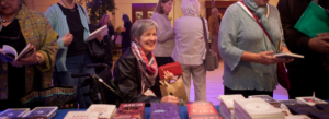 A woman in a wheelchair, smiling, in front of a table of books