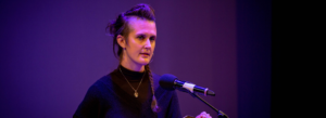 Image of woman in a black top stood speaking into a microphone